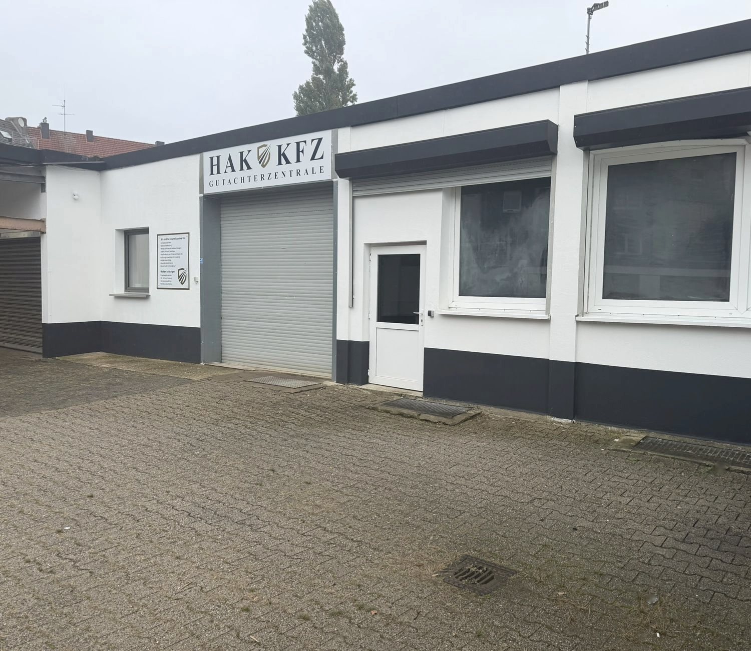 Seitenansicht der HAK KFZ Gutachterzentrale mit Hallentor, Büro und gepflastertem Hof